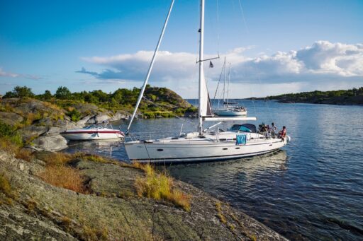 Vit segelbåt och motorbåt förtöjd till klippor