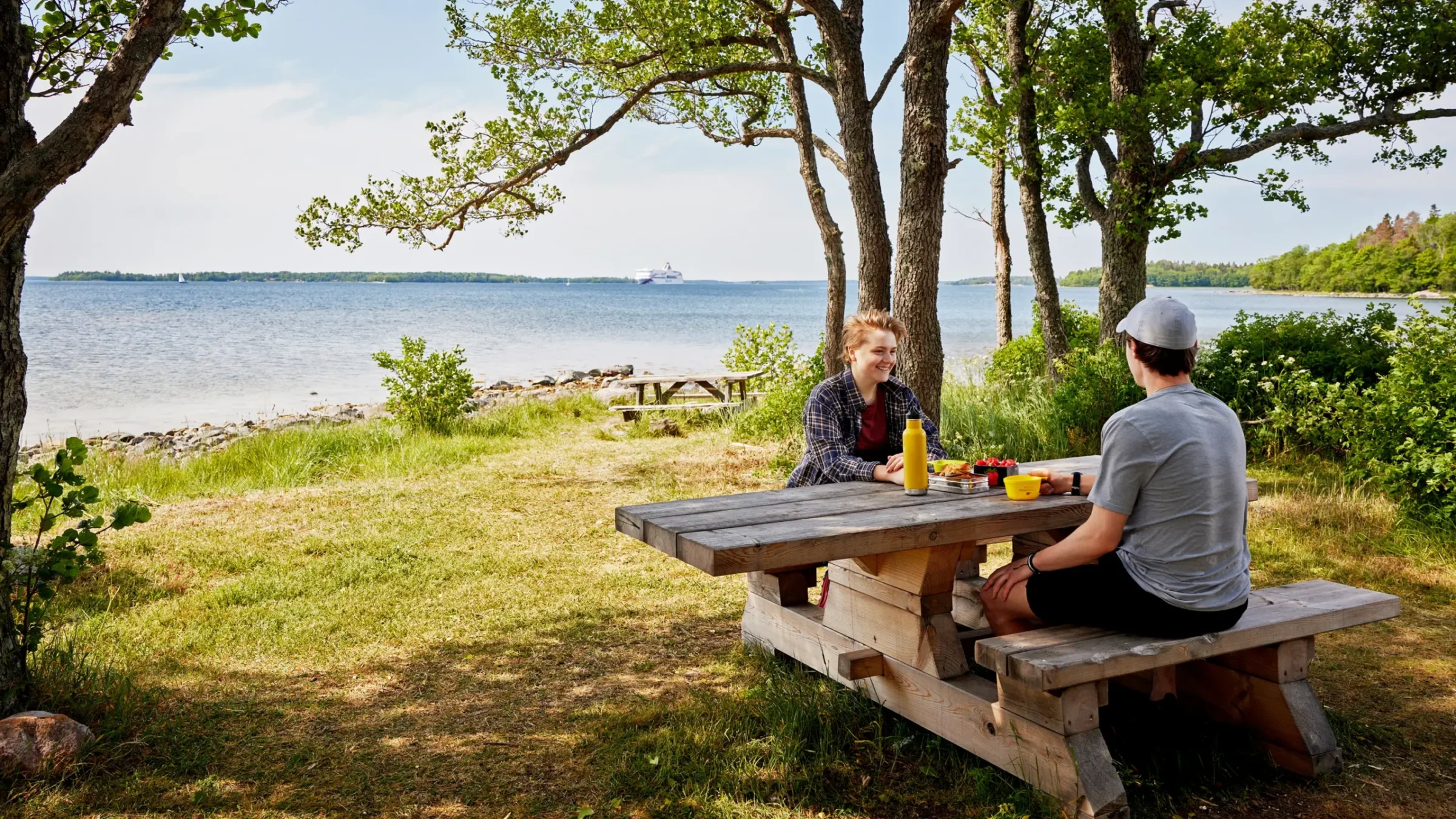 Människor sitter på bänk vid strand på Ridderholm